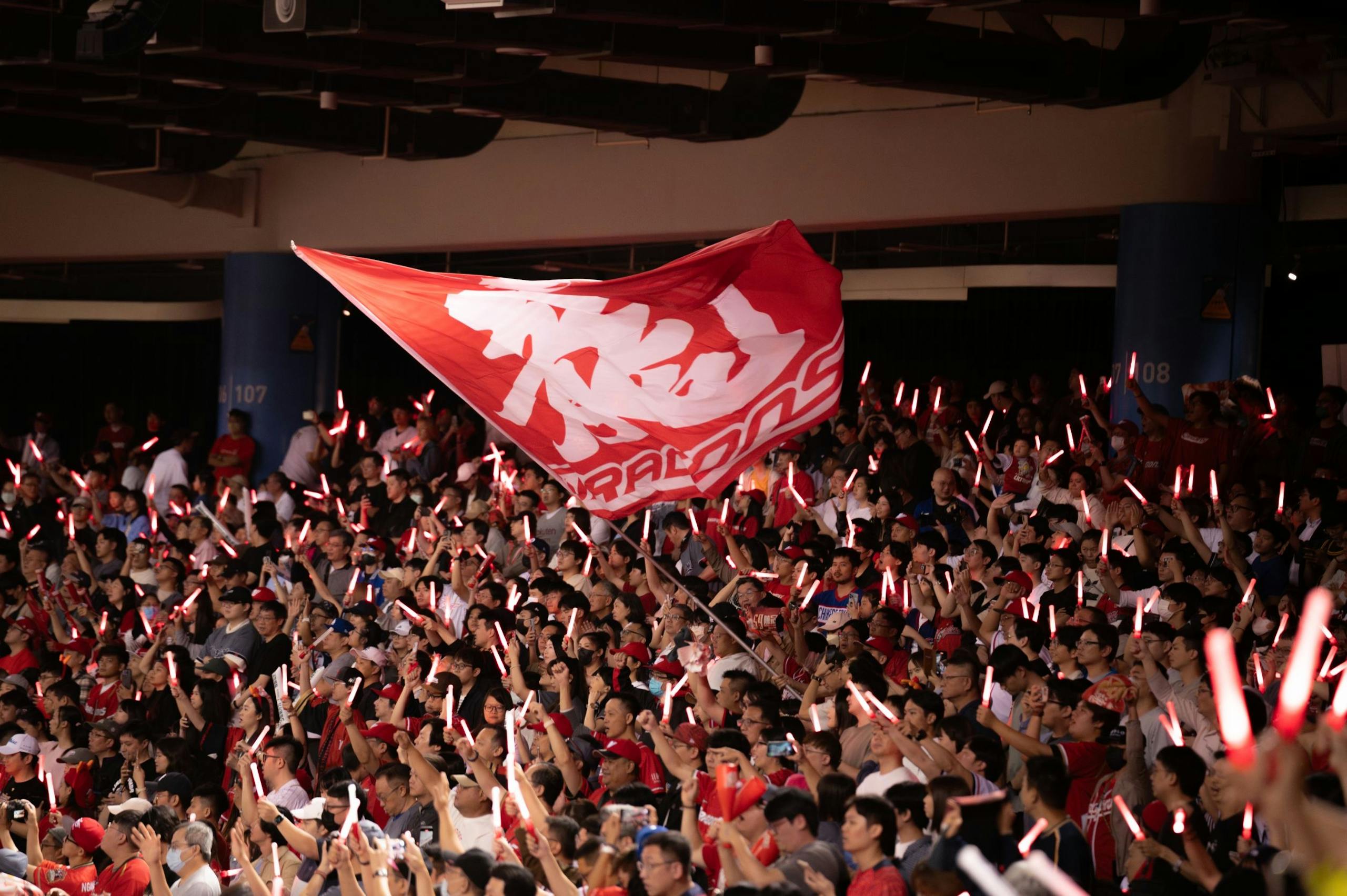 Vibrant crowd waving a flag with glowing sticks at a Taipei sports event, showcasing excitement and unity.
